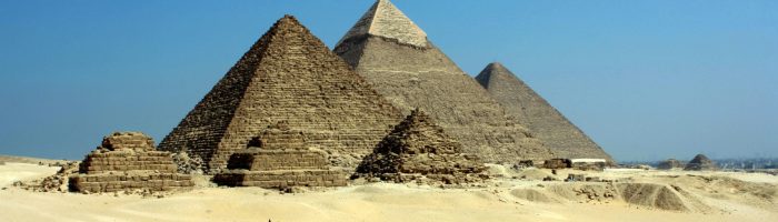 Capture of the iconic Pyramids of Giza under a clear blue sky with camels traversing the sandy desert.